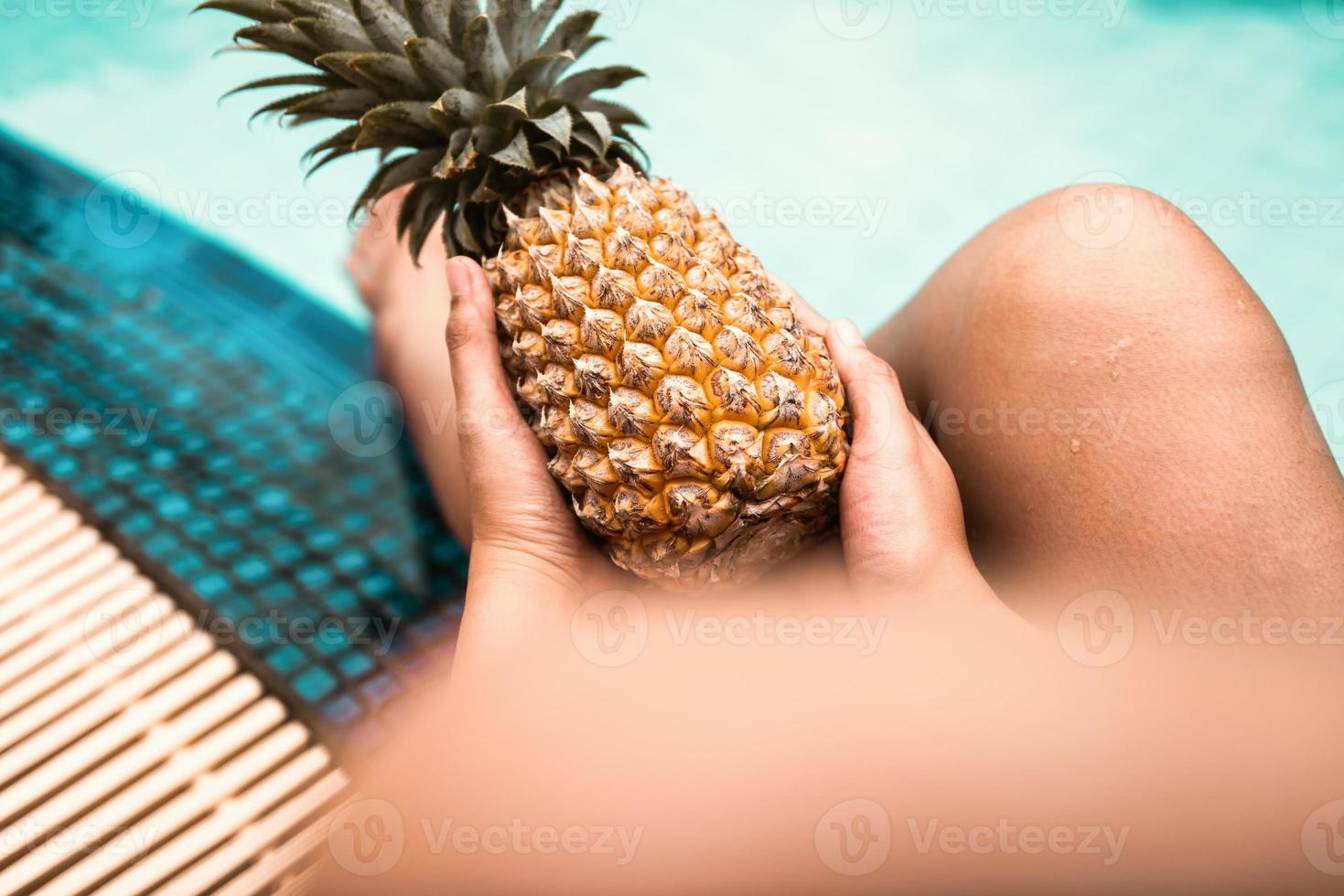 La mujer se está relajando en la piscina mientras sostiene la piña foto