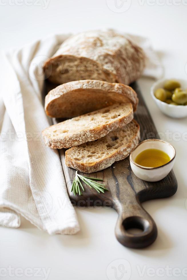 hogaza de pan en rodajas sobre una tabla de cortar. aceite de oliva, aceitunas y albahaca foto