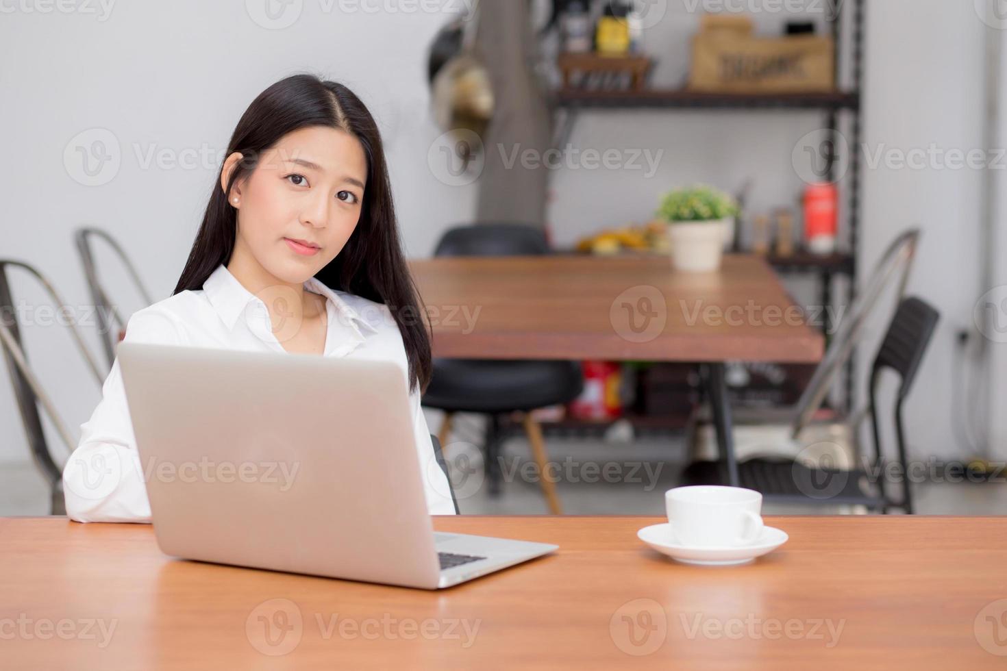 mujer asiática joven que trabaja en línea en la computadora portátil que se sienta en el café. foto