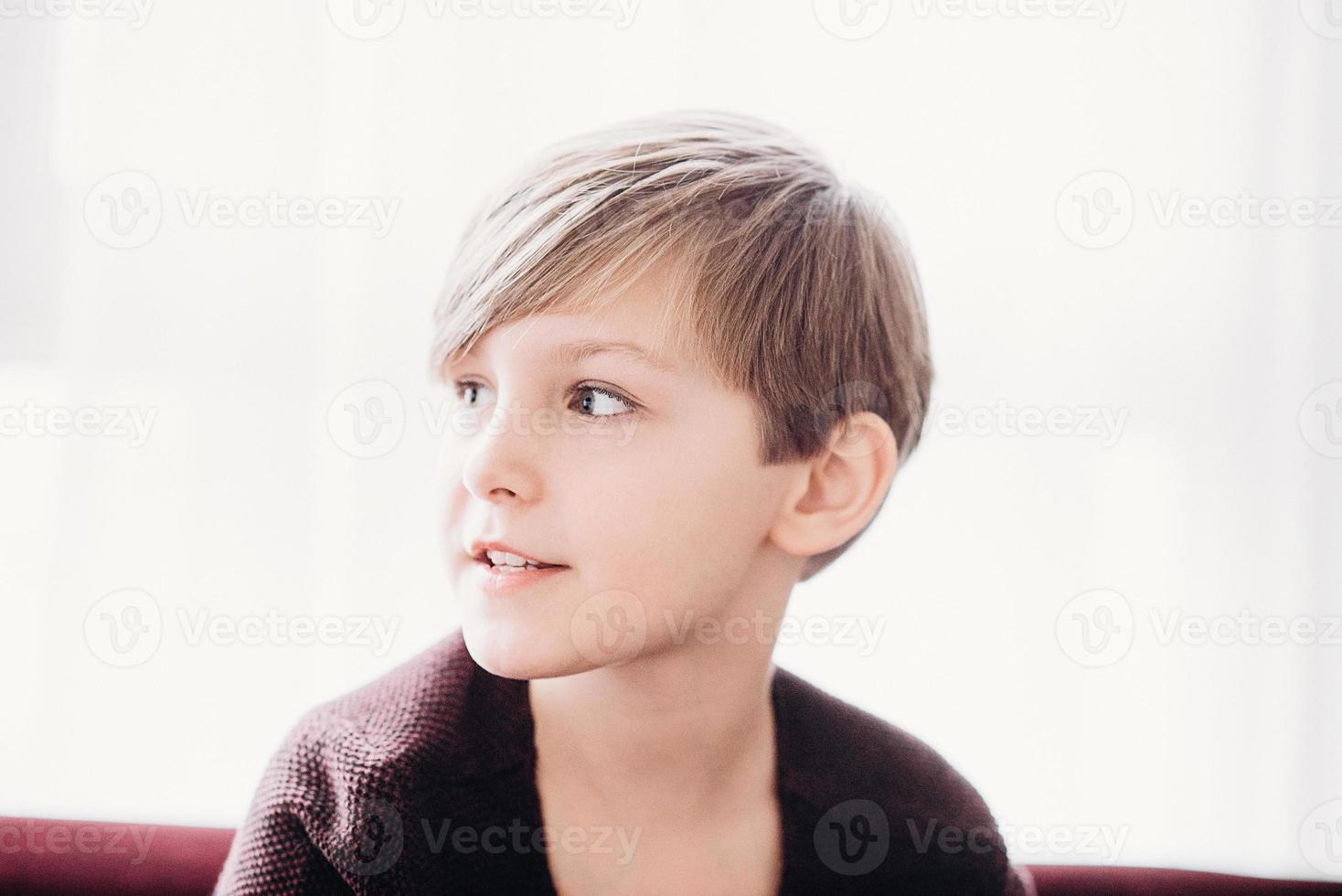 A closeup portrait of a cute boy kid sitting on a sofa against the light window, soft focus photo