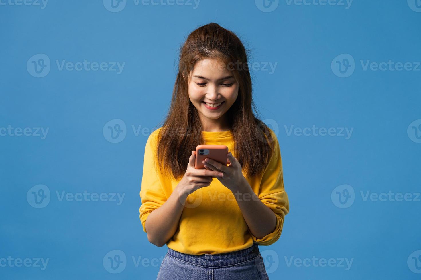 Señora asiática que usa el teléfono con expresión positiva sobre fondo azul. foto