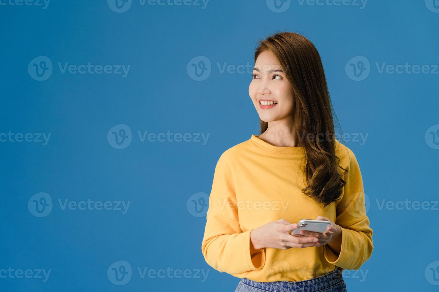 Young lady using phone with positive expression on blue background. photo