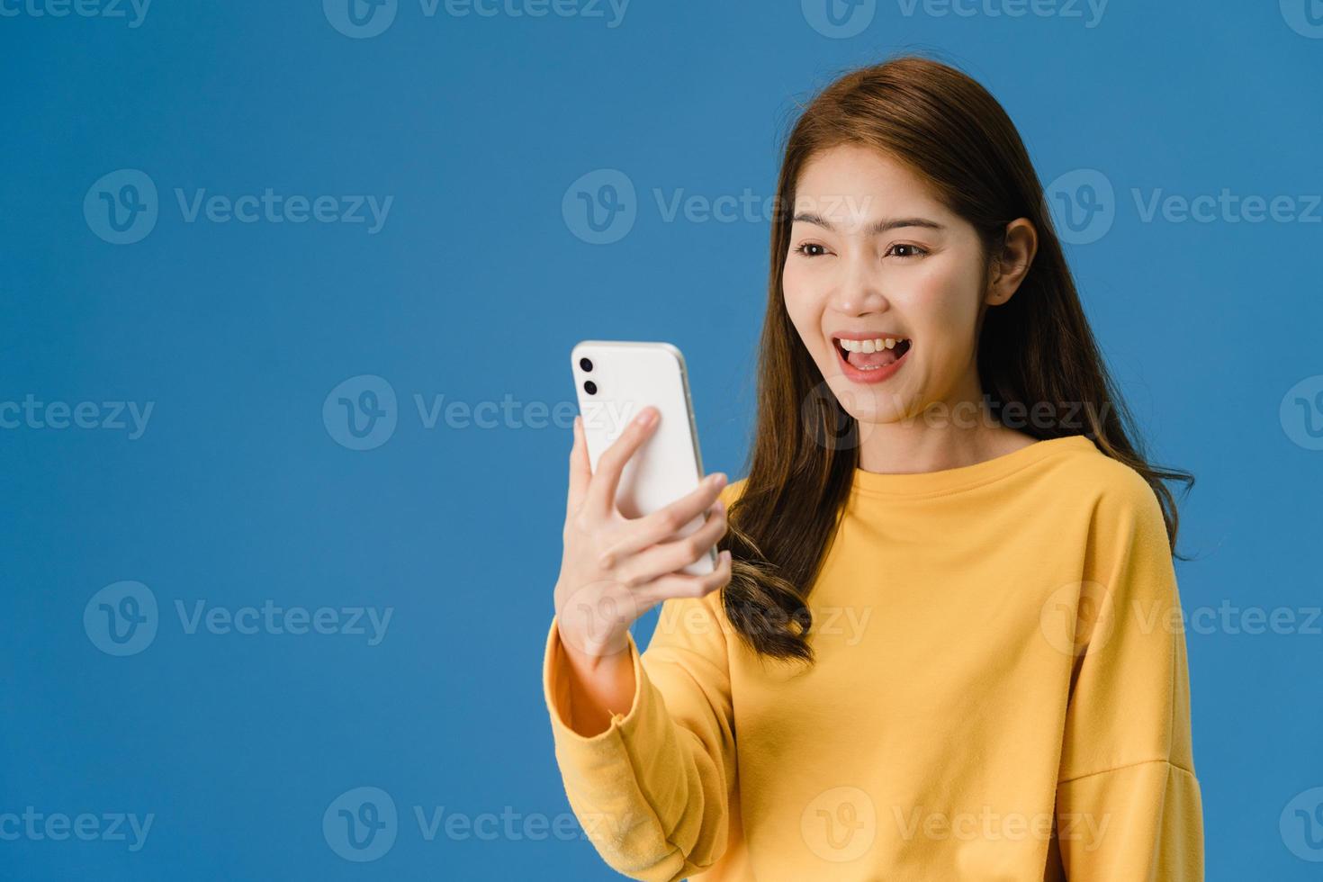 Señora asiática que usa el teléfono con expresión positiva sobre fondo azul. foto