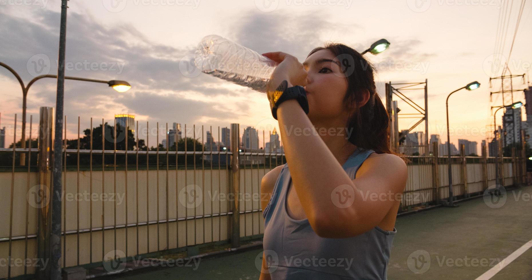 Asia atleta dama ejercicios de agua potable después de correr. foto