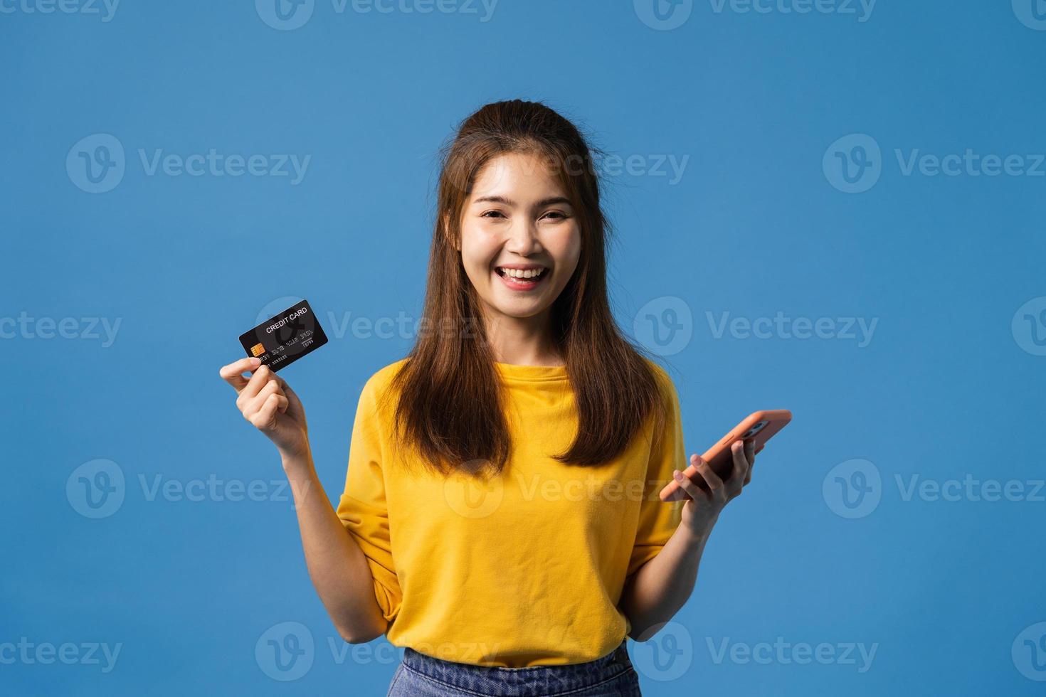 Jovencita asiática con teléfono y tarjeta bancaria de crédito sobre fondo azul. foto