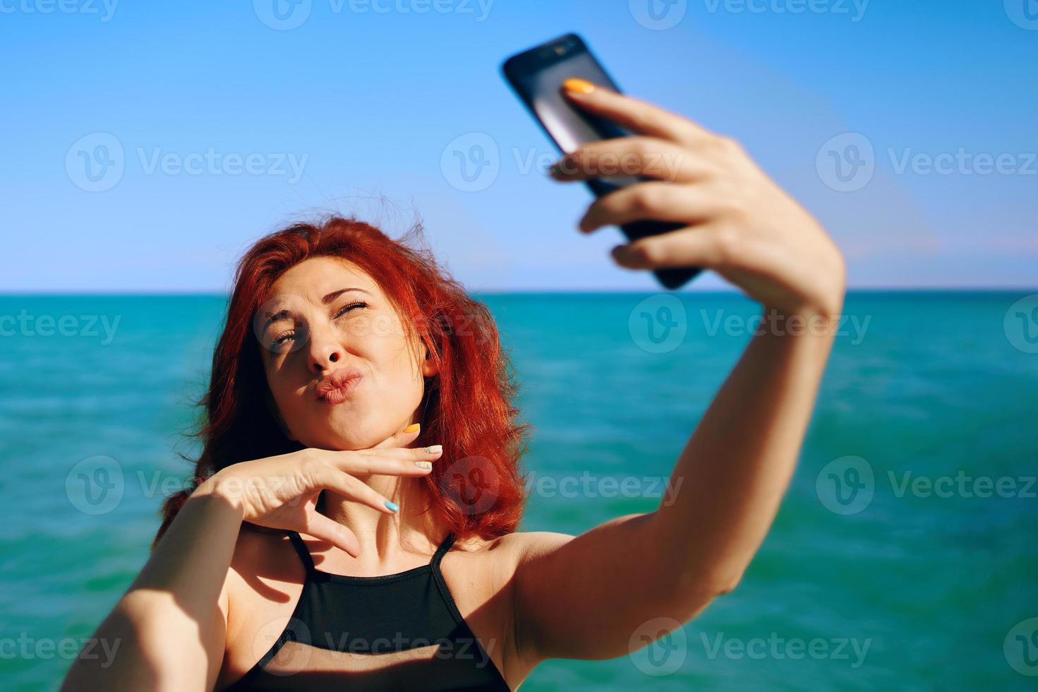 Mujer pelirroja toma selfie en la cámara del teléfono inteligente foto