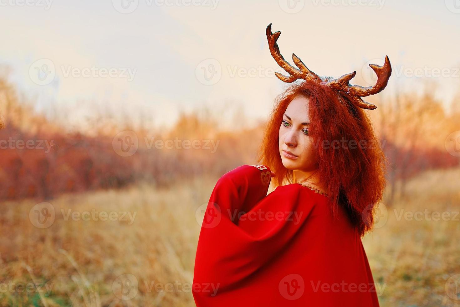 Mujer en vestido largo rojo con cuernos de ciervo en el bosque de otoño foto