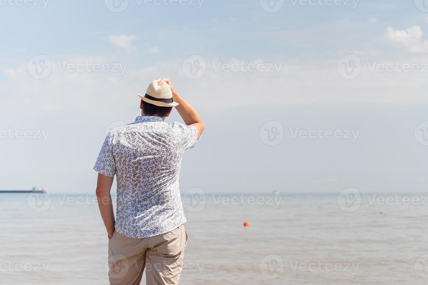 Joven en ropa de verano de pie en un muelle, el mar al fondo foto