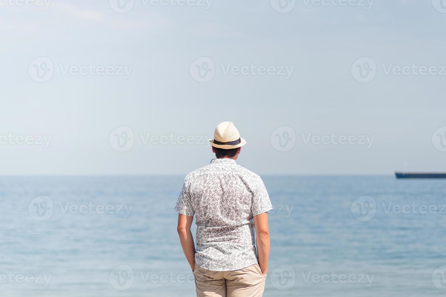 Joven en ropa de verano de pie en un muelle, el mar al fondo foto