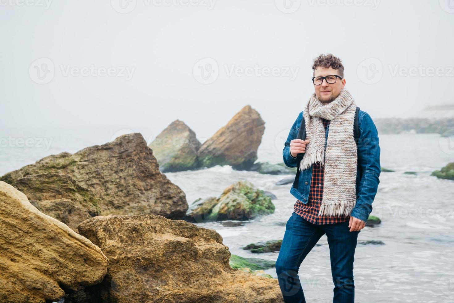 Hombre con una mochila de pie sobre una roca frente a un hermoso mar foto
