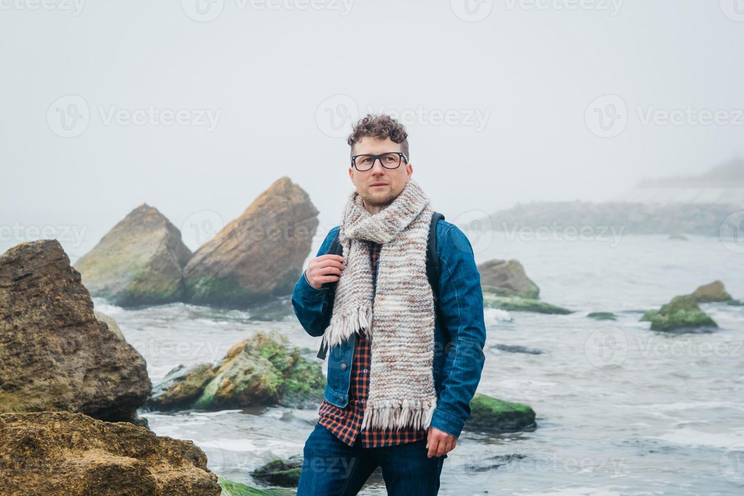 Hombre con una mochila de pie sobre una roca frente a un hermoso mar foto