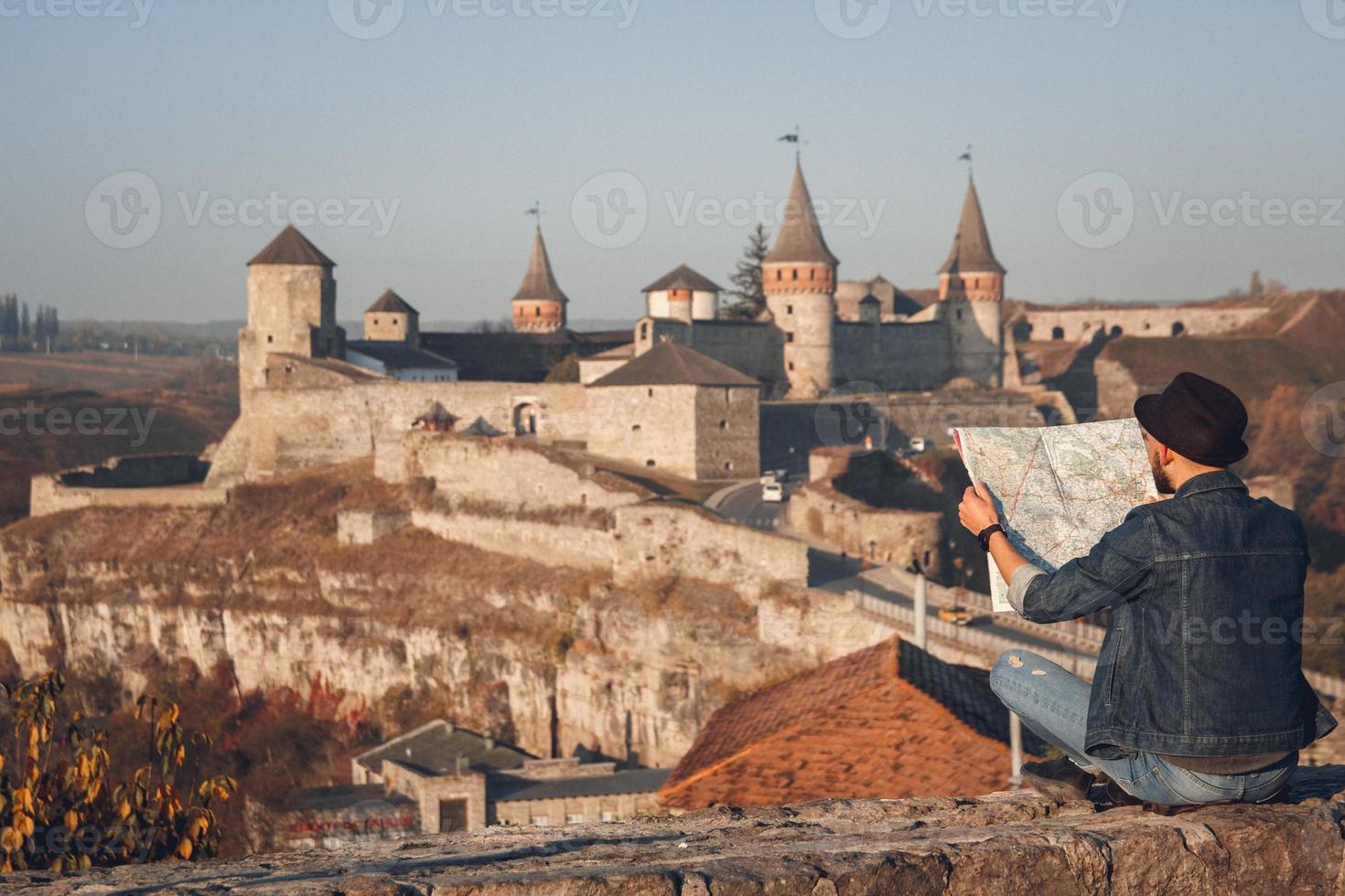 Hombre viajero con un mapa en sus manos se sienta en el fondo del antiguo castillo foto