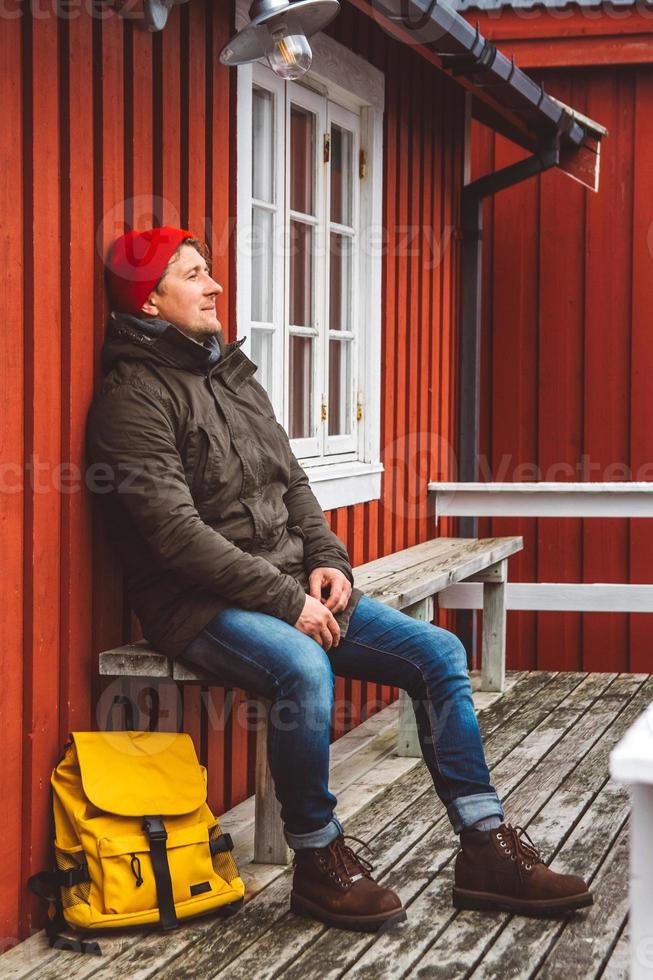 hombre viajero se sienta cerca de la casa de madera de color rojo foto