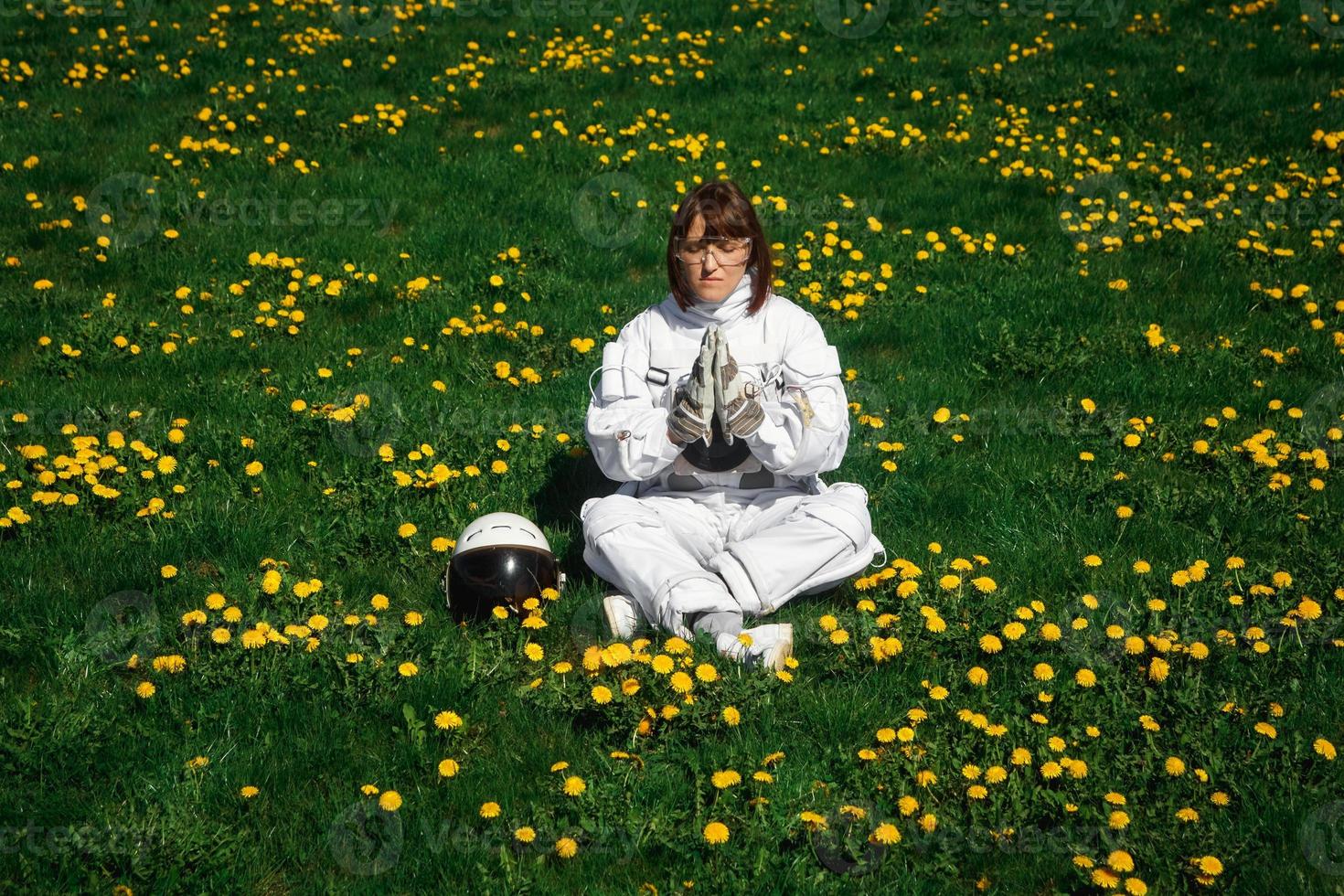 Mujer astronauta sin casco se sienta en un césped verde entre flores foto