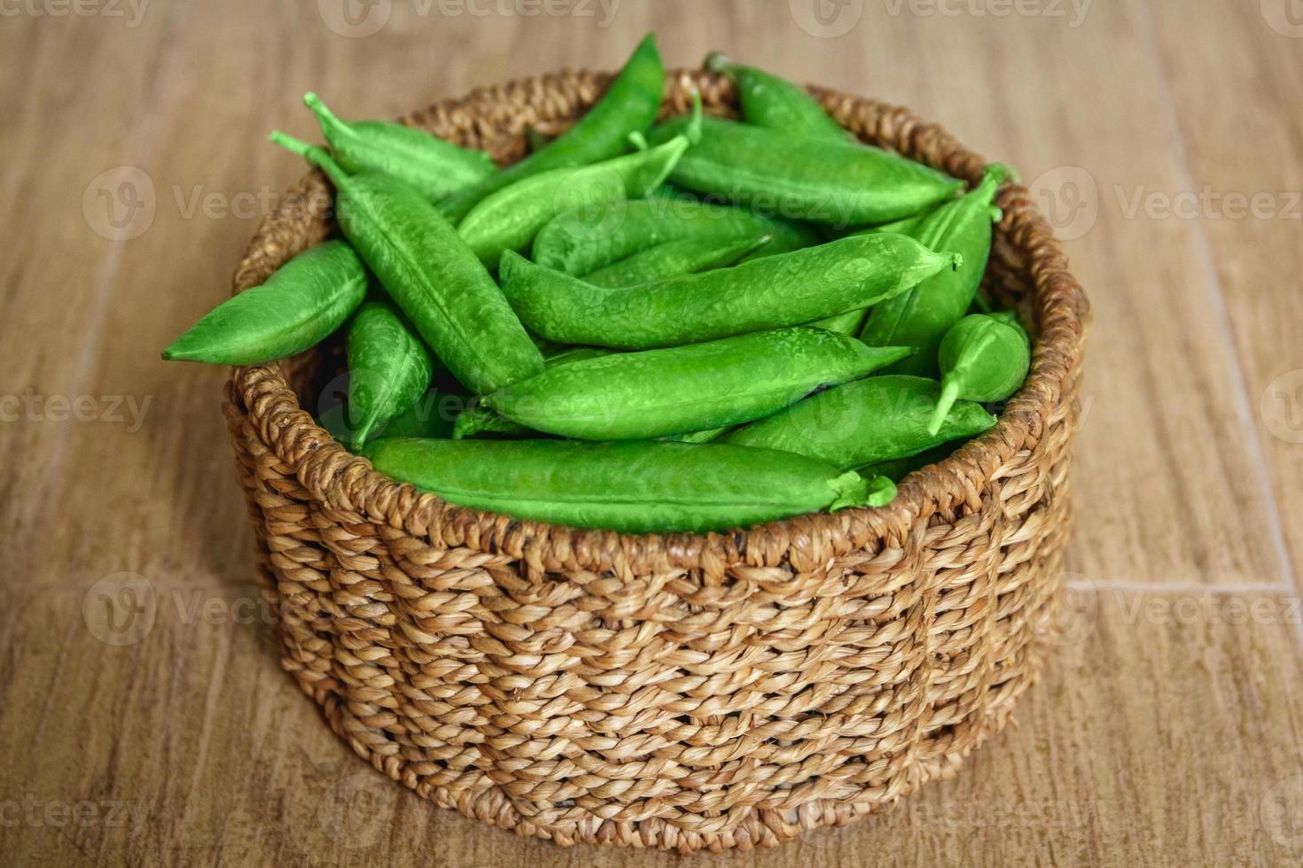 The crop of peas lies in a round wicker basket on a wooden background photo