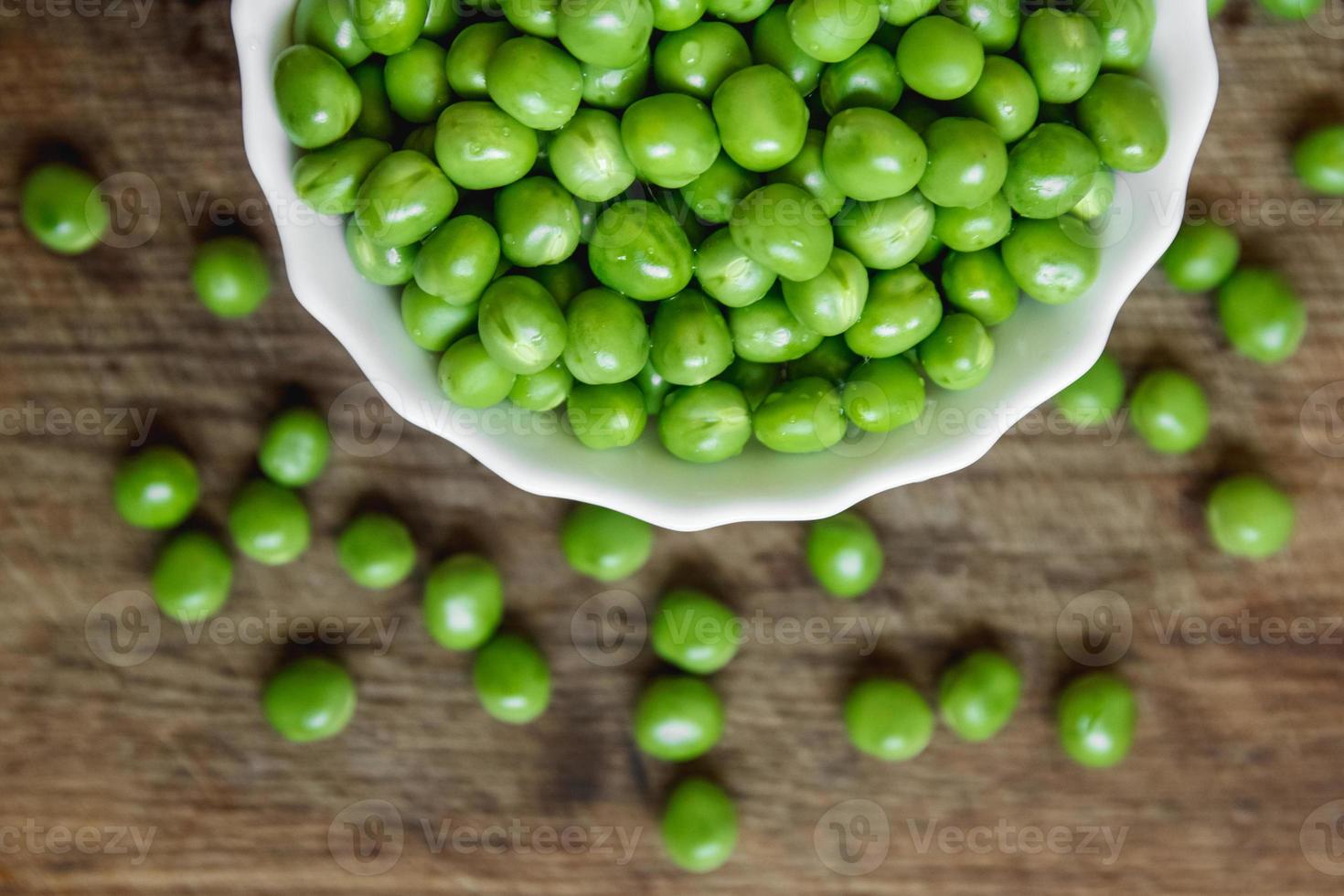 Guisantes verdes frescos en un plato blanco sobre fondo de madera, vista superior foto