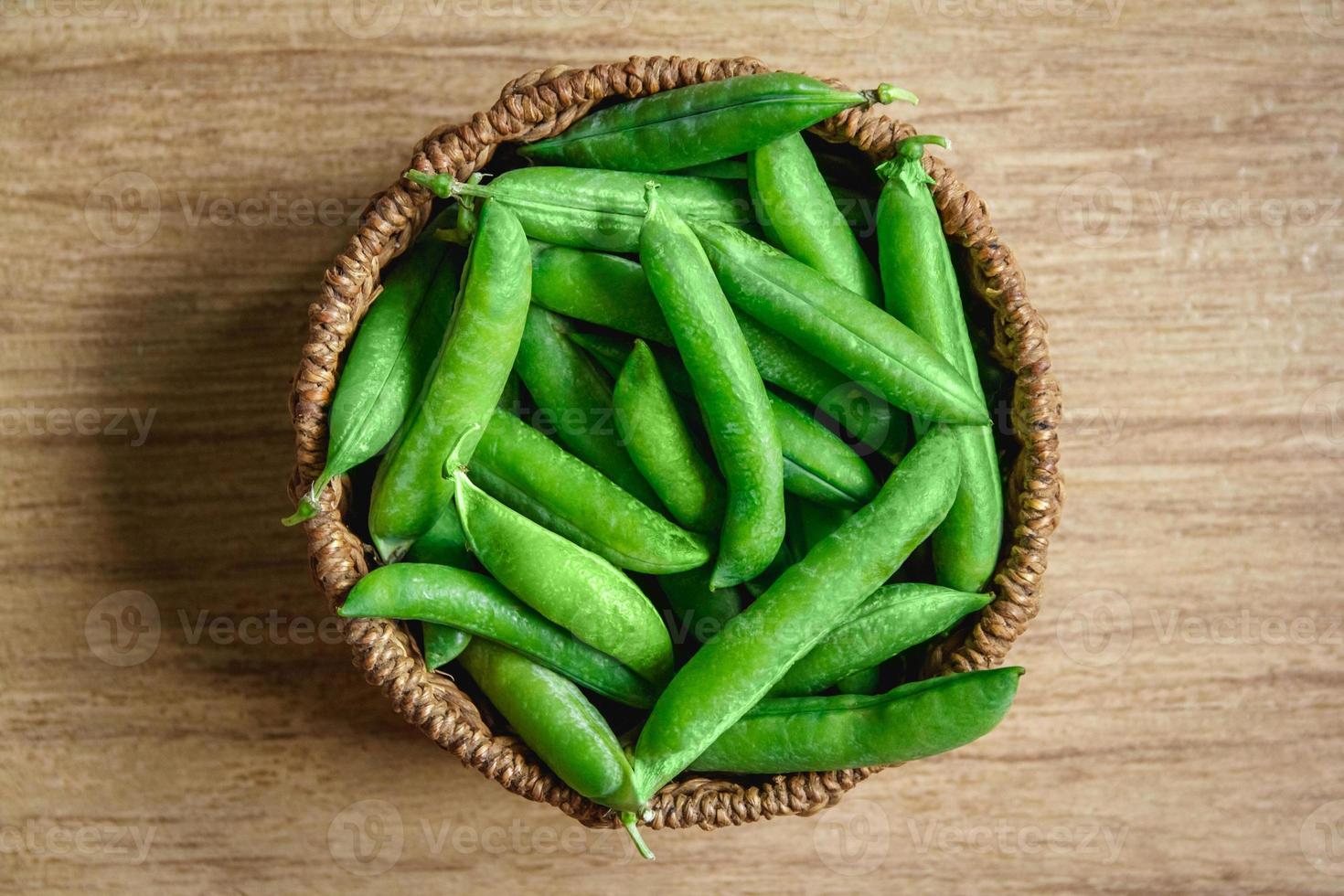 The crop of peas lies in a round wicker basket on a wooden background photo