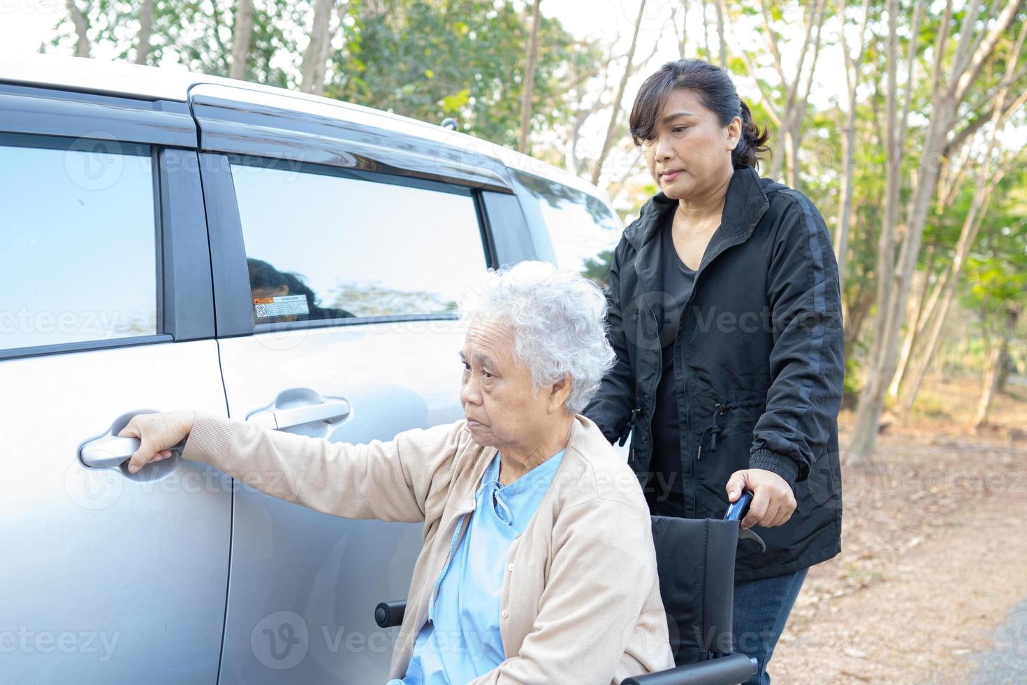 Ayudar a paciente mujer mayor asiática sentada en silla de ruedas al coche foto