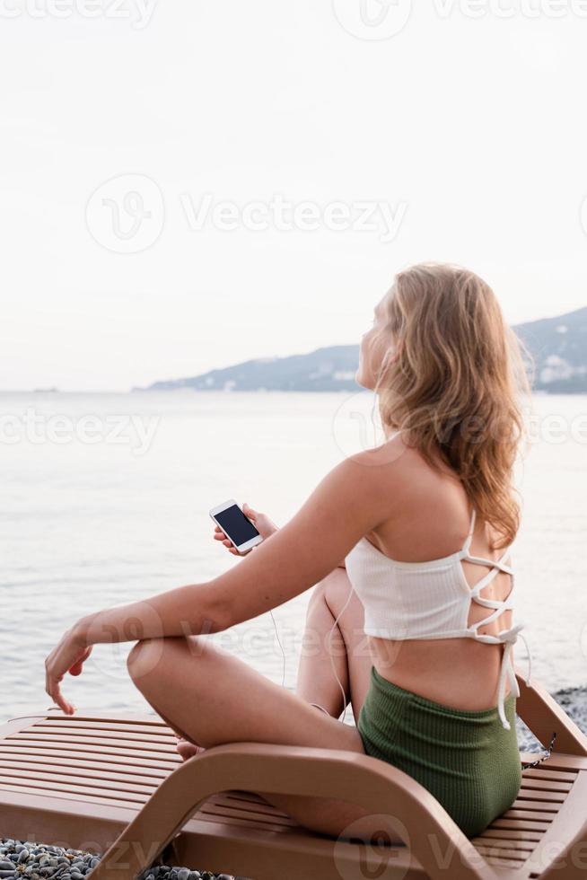 Woman sitting on the sun lounger listening to the music and dancing photo