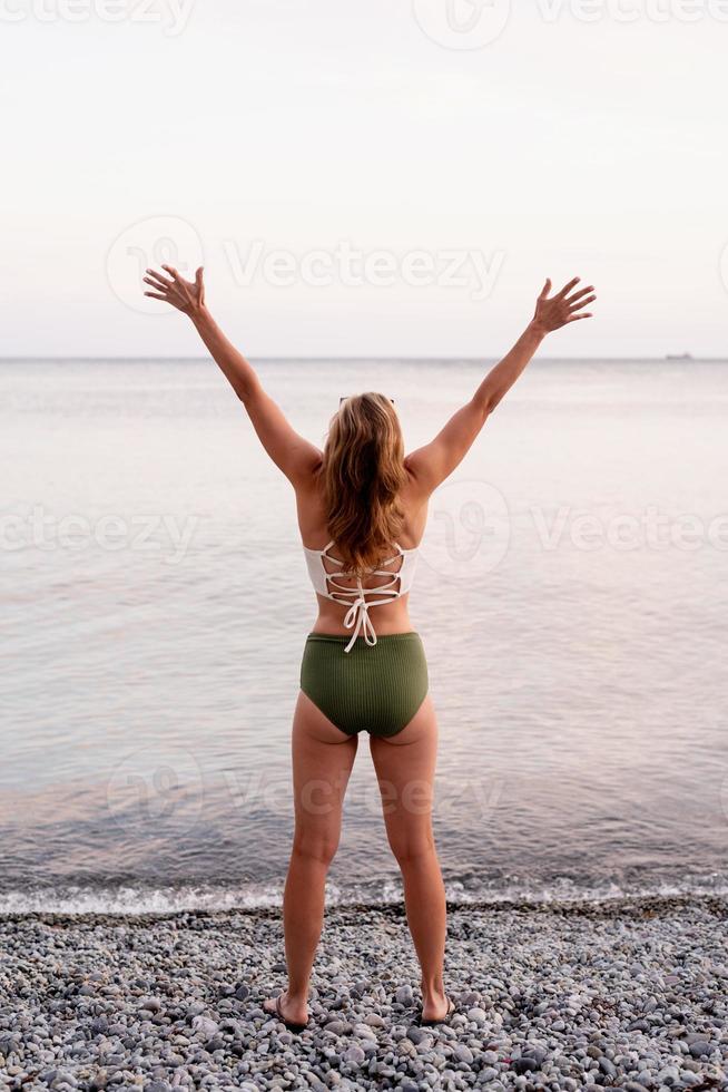 Young woman standing on stony beach with outstretched arms dancing photo