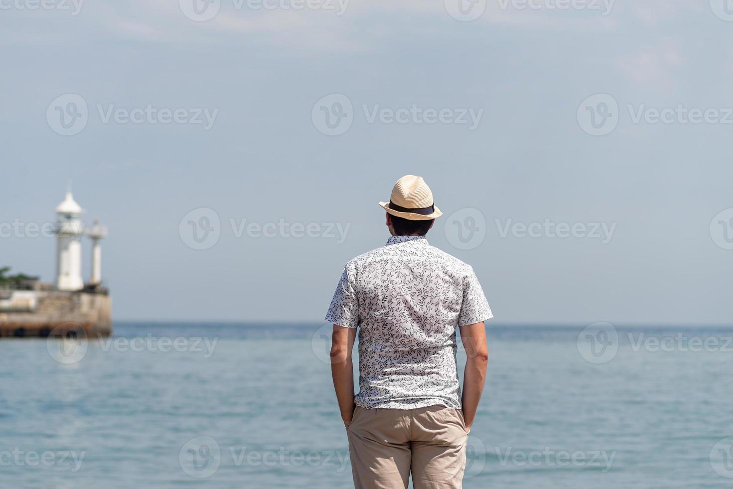 Hombre de pie en el muelle con el mar y el faro en el fondo foto