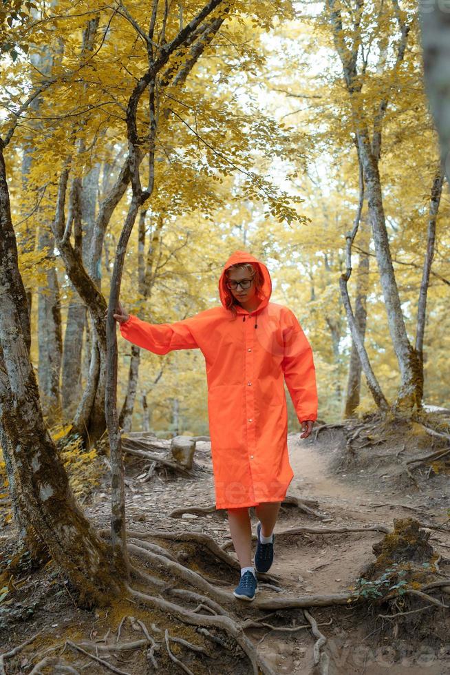 Mujer feliz en impermeable naranja caminando en el bosque foto