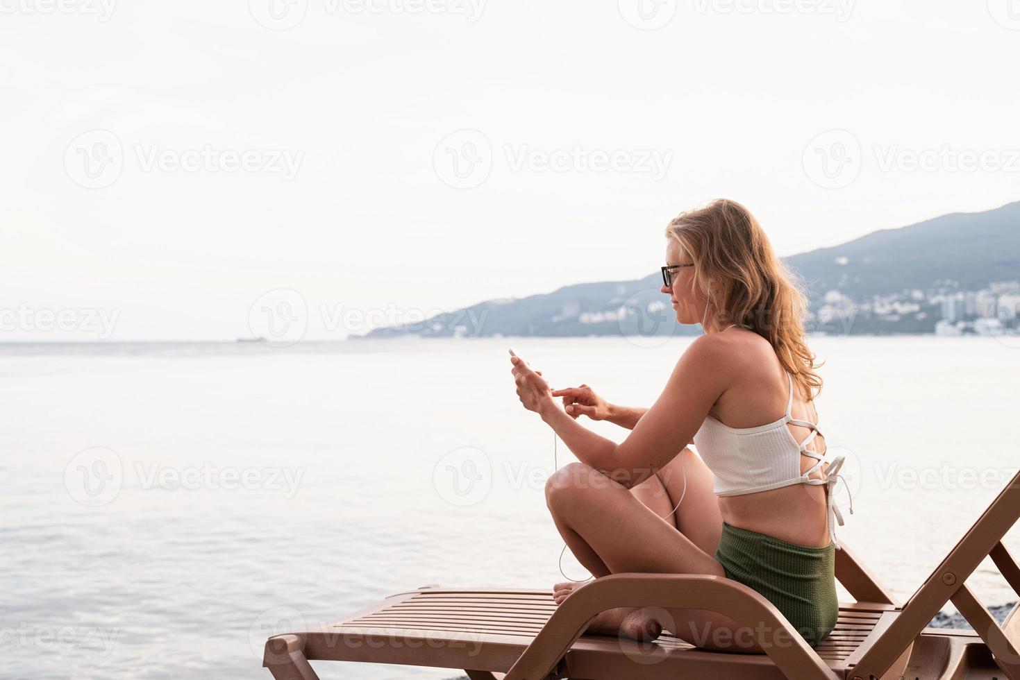 Mujer joven sentada en la tumbona escuchando música foto