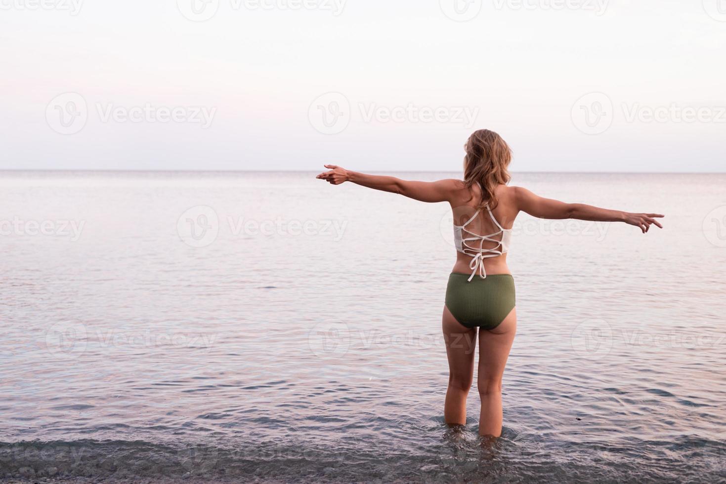 young woman standing on stony beach with outstretched arms photo