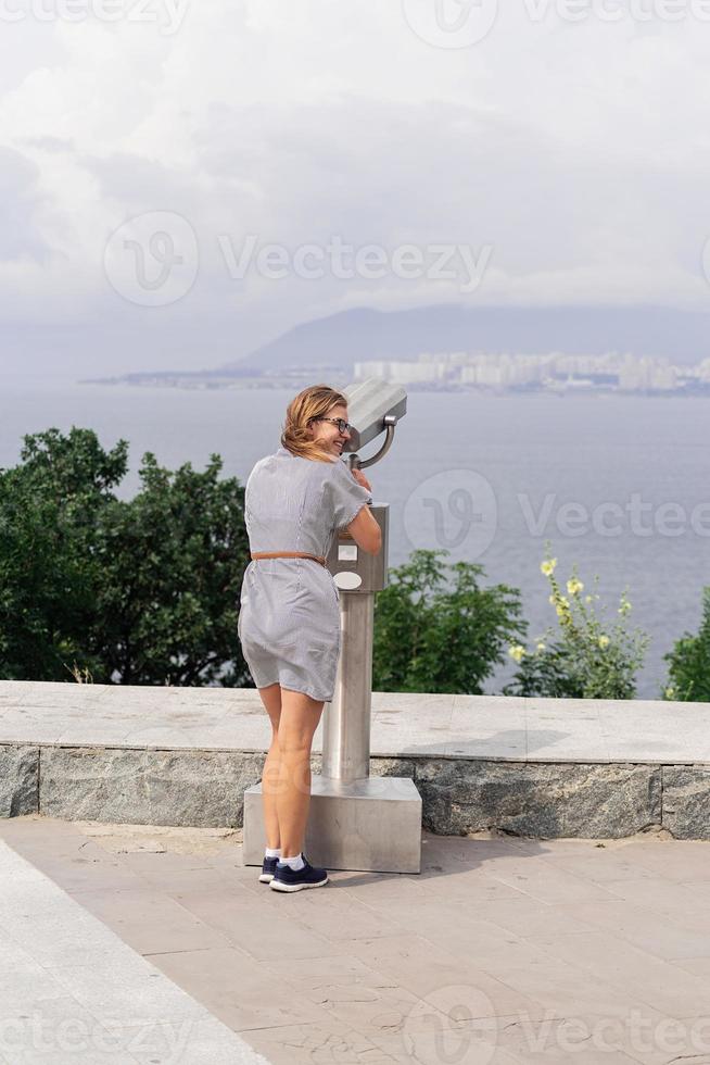 Mujer con binoculares estacionarios contra el fondo del mar y la ciudad foto