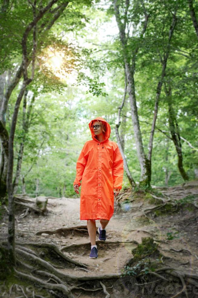 Mujer feliz en impermeable naranja caminando en el bosque foto