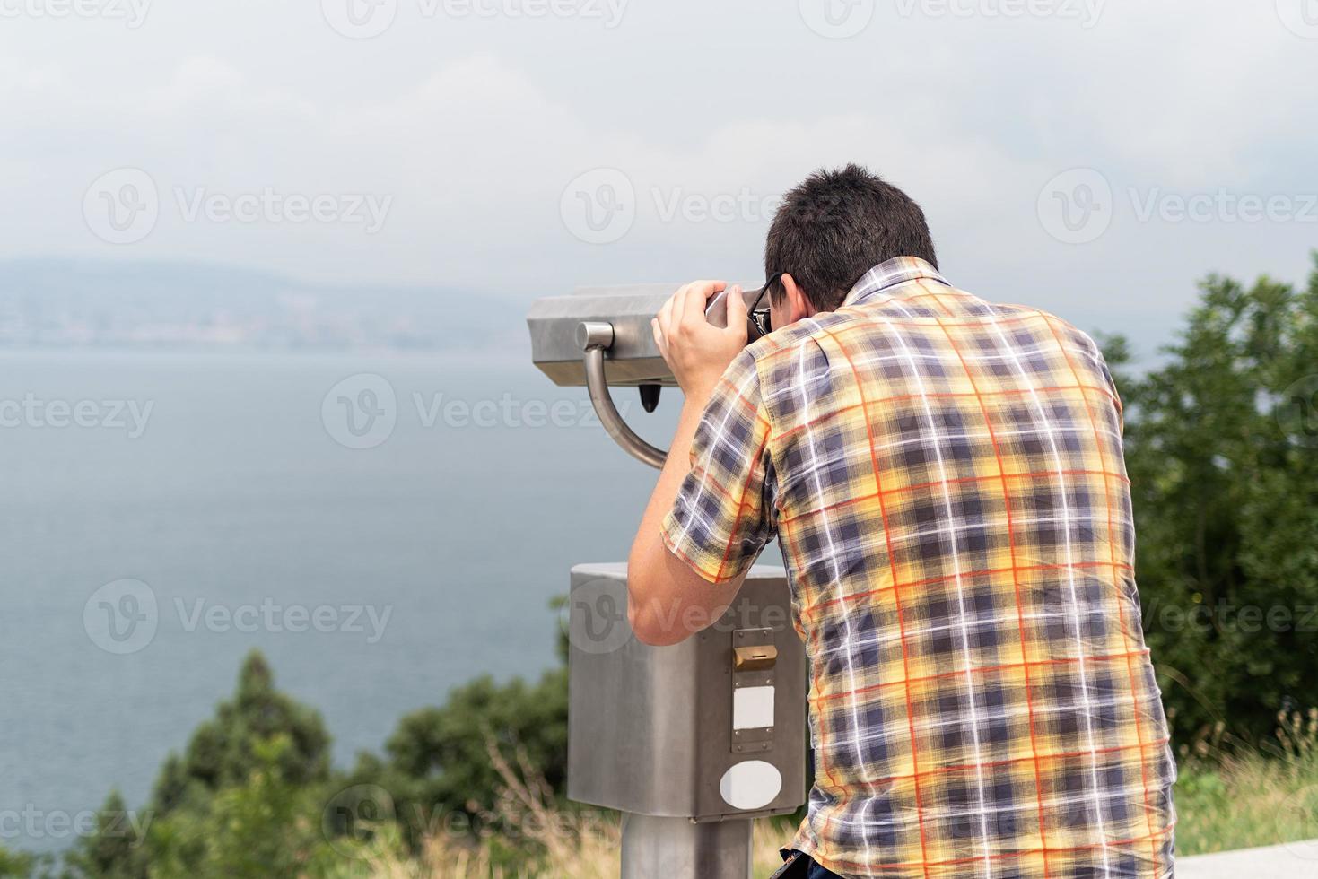 Joven con binoculares estacionarios de las montañas y el mar foto