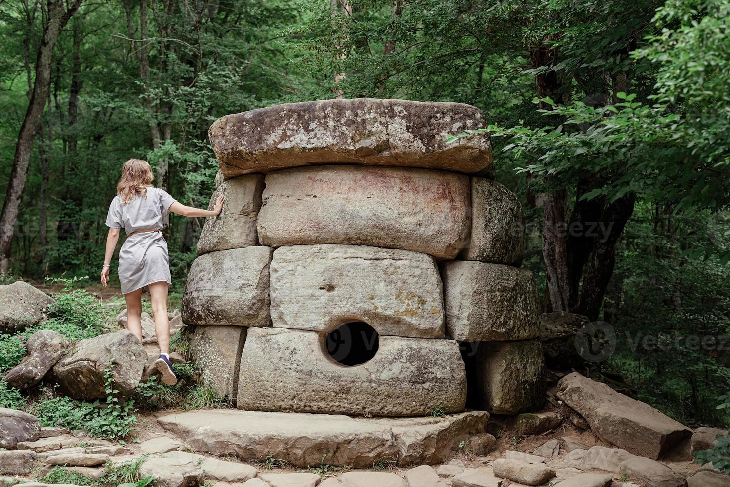 Woman in summer dress walking near big dolmen stone in the forest photo