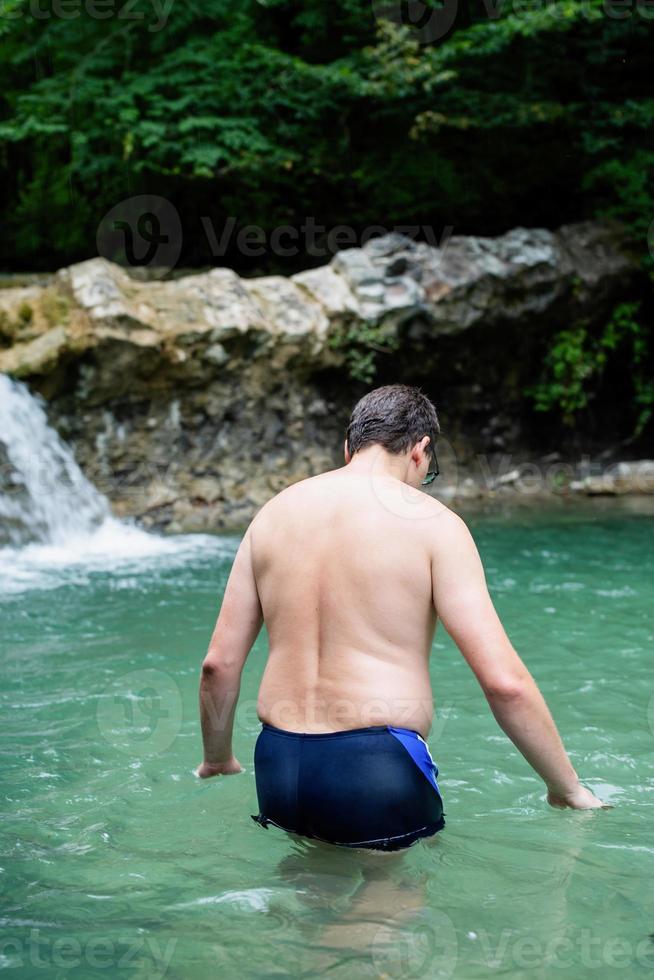 Hombre nadando en el río de la montaña con una cascada. foto