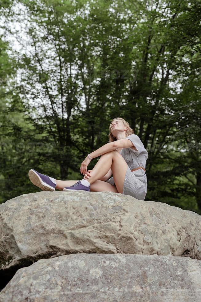 Mujer joven sentada sobre una piedra grande en el bosque mirando a otro lado foto