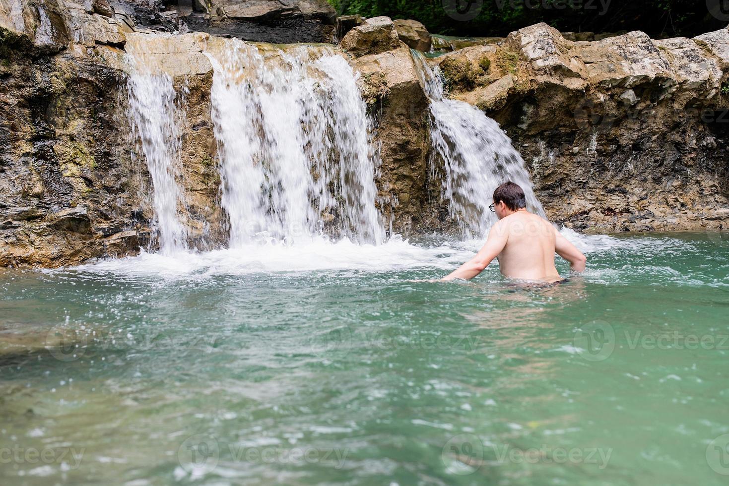 Hombre nadando en el río de la montaña con una cascada. foto