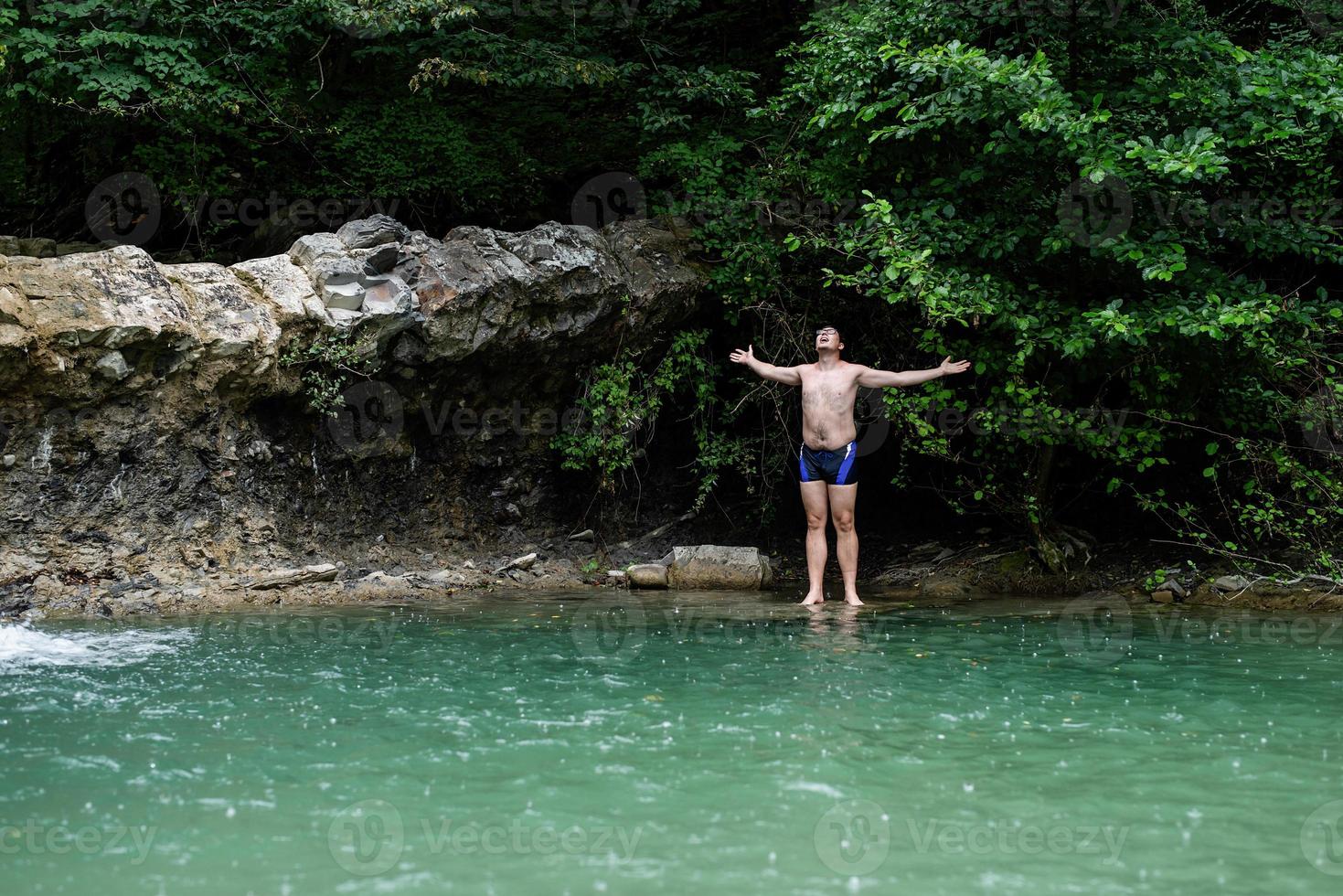 Hombre nadando en el río de la montaña con una cascada. foto