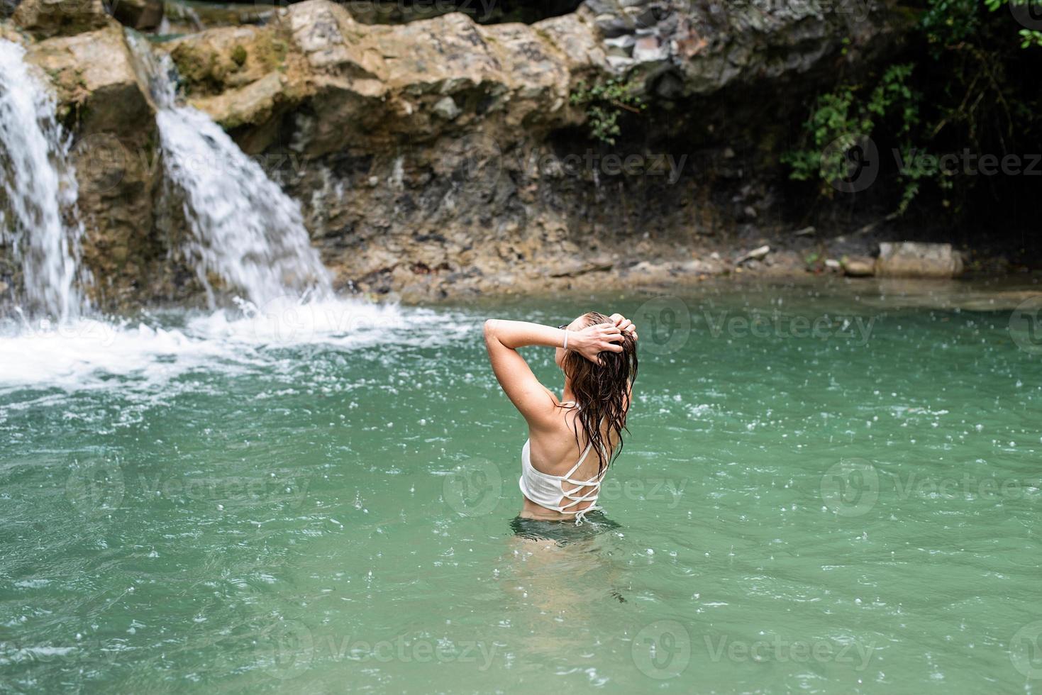 Woman swimming in the mountain river with a waterfall photo