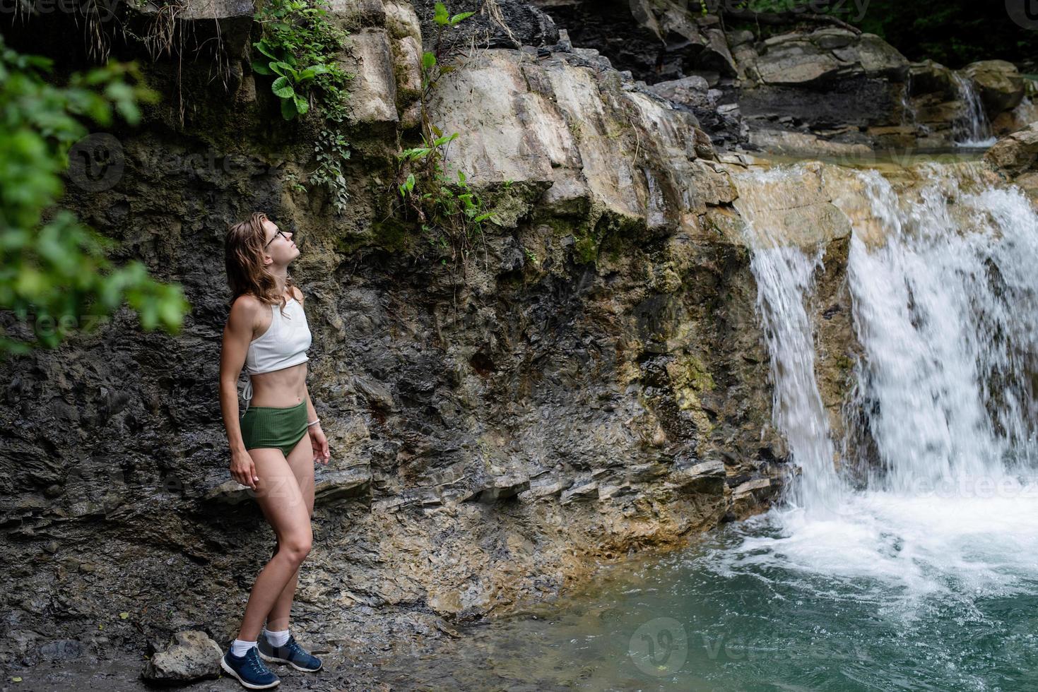 Young sexy woman in swimsuit enjoing the waterfall photo