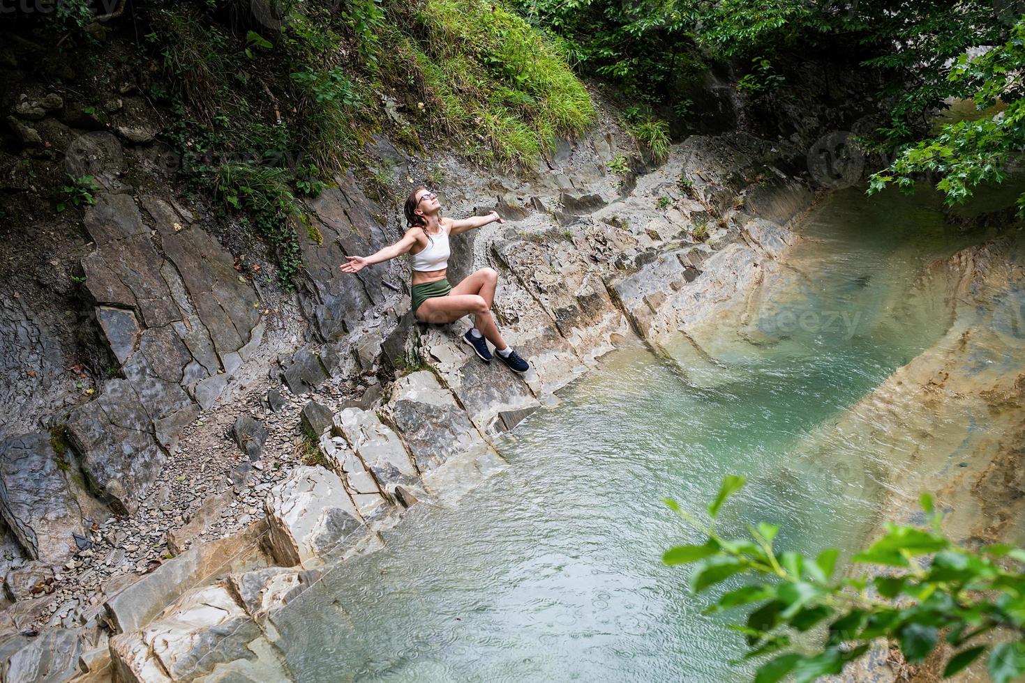 joven feliz disfrutando de la naturaleza, sentada junto al río de la montaña. foto