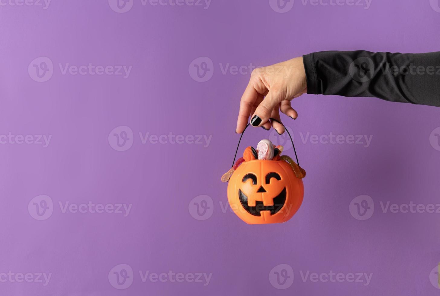 mano de halloween con uñas negras sosteniendo calabaza llena de dulces foto