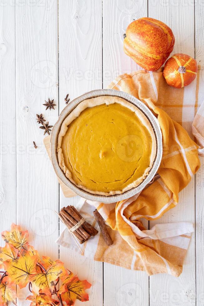 Homemade pumpkin pie with autumn leaves on rustic background, top view photo