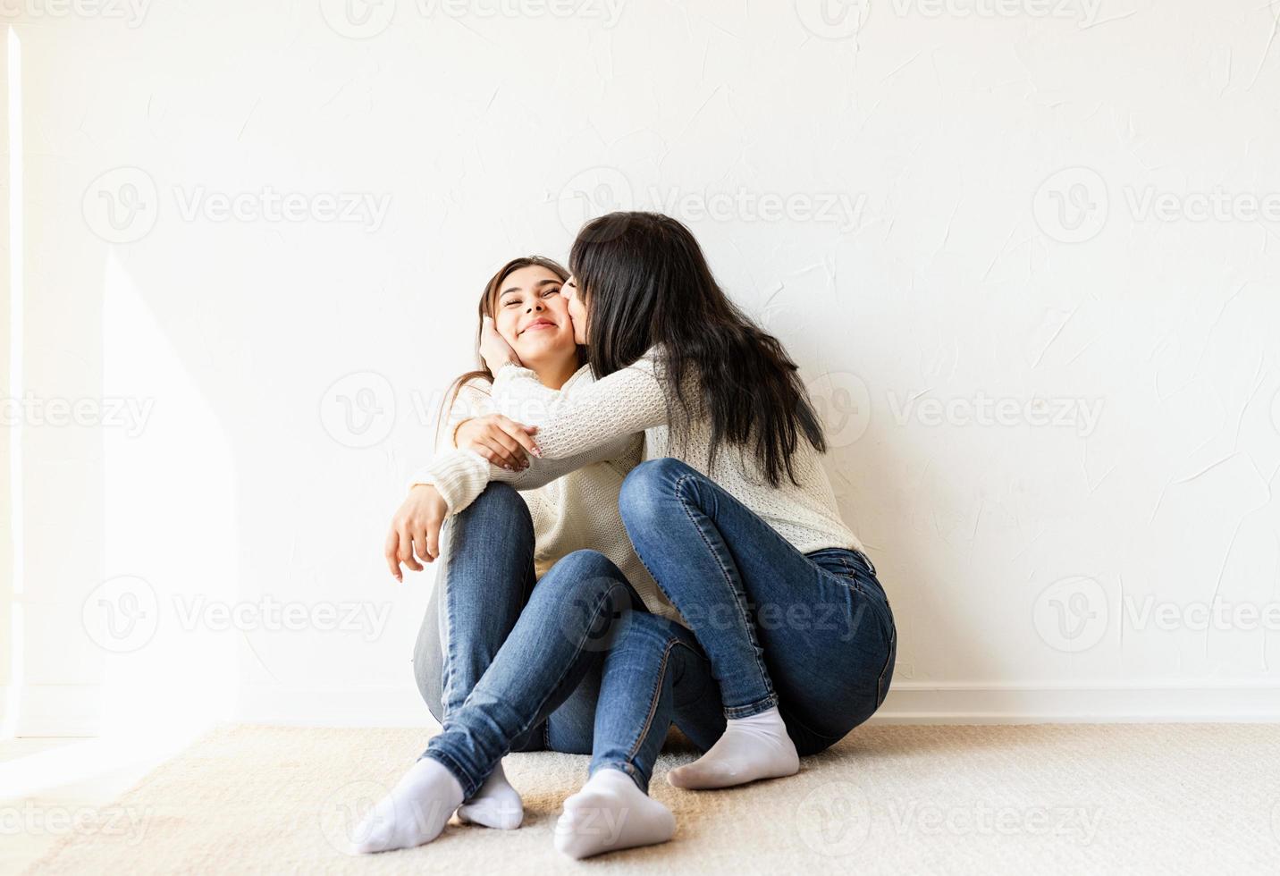 Two female best friends sitting together at home kissing each other photo