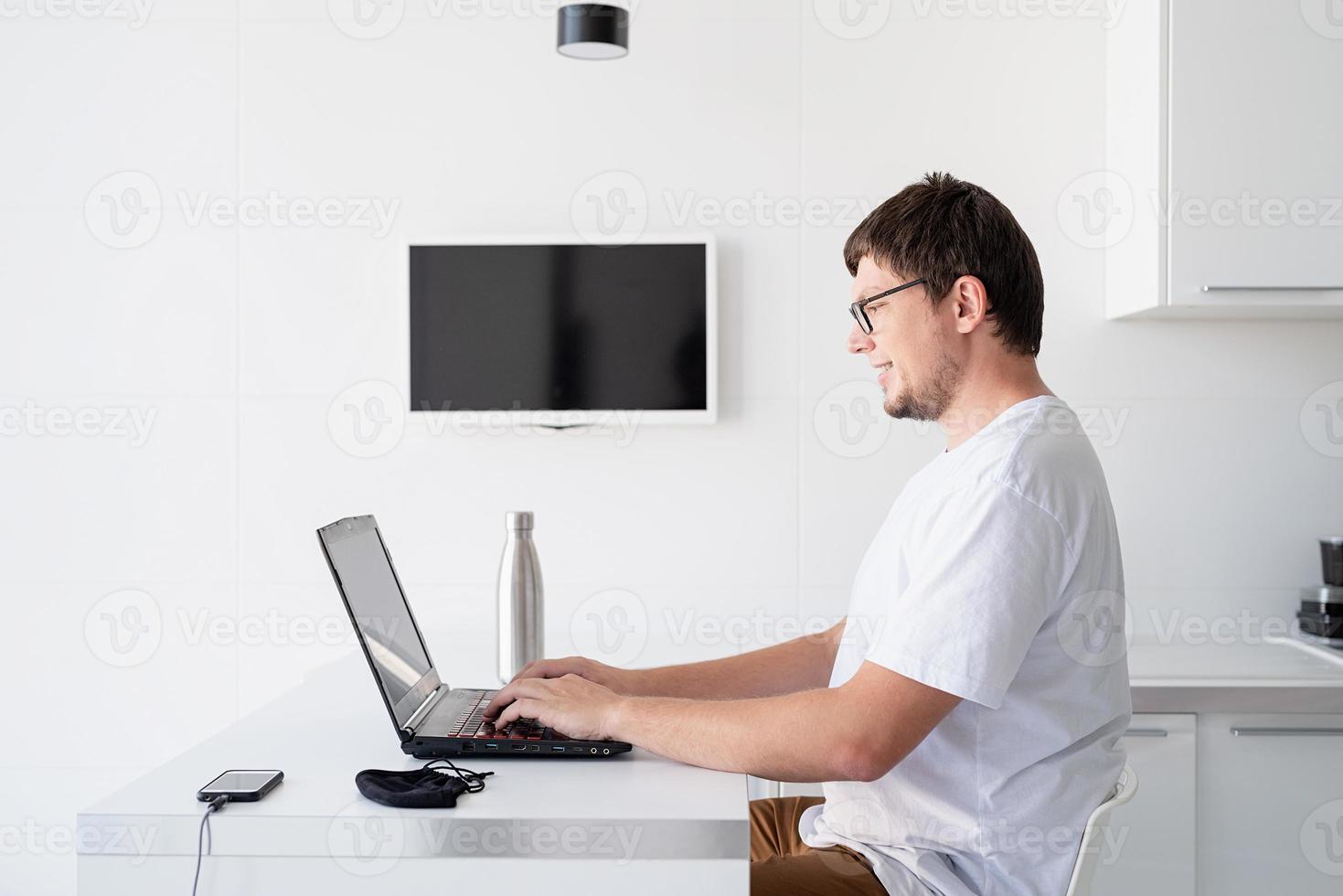 Young smiling man working with laptop from home photo