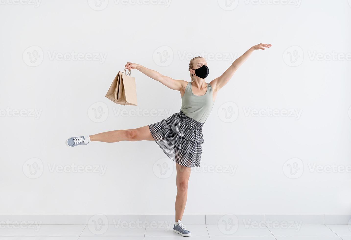 Mujer joven bailando ballet con bolsas de la compra en una máscara protectora foto