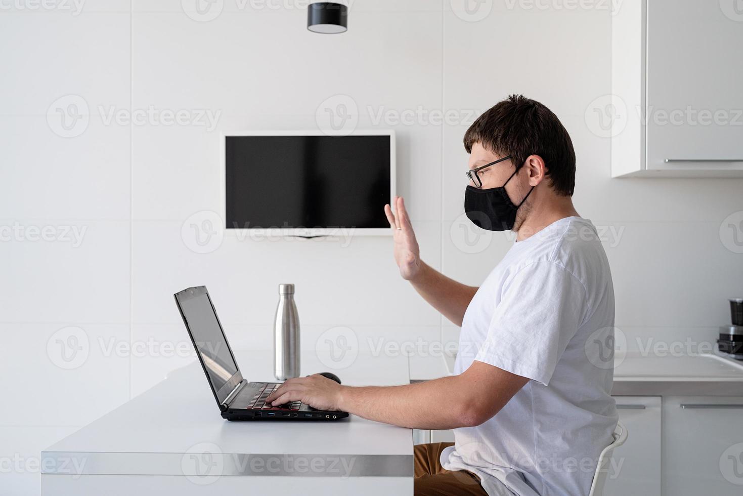 Young man in black protective mask working with laptop from home photo