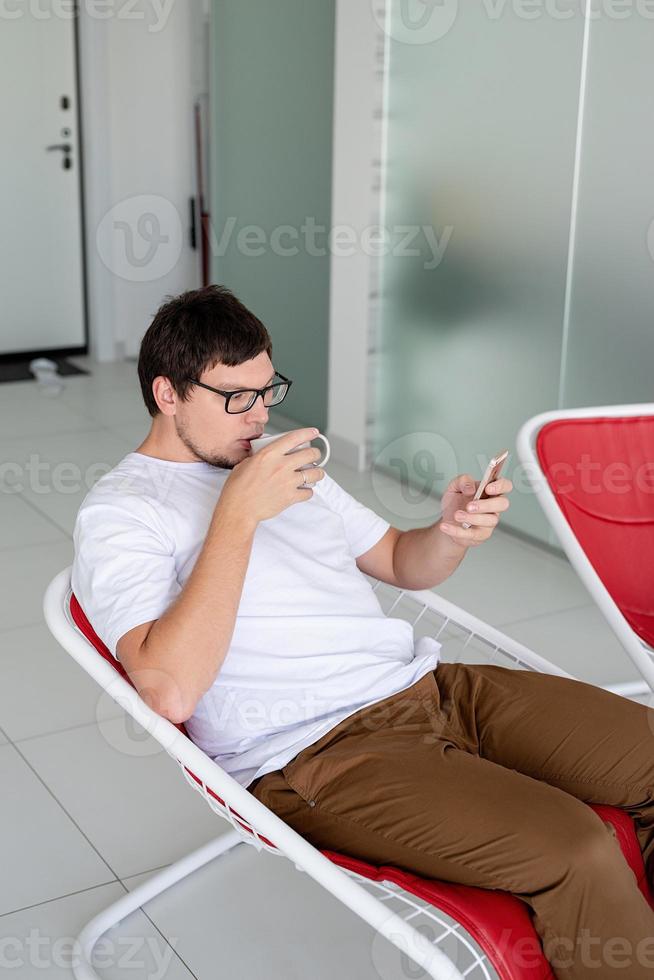 Man sitting in a chair watching tv holding tea cup and phone photo