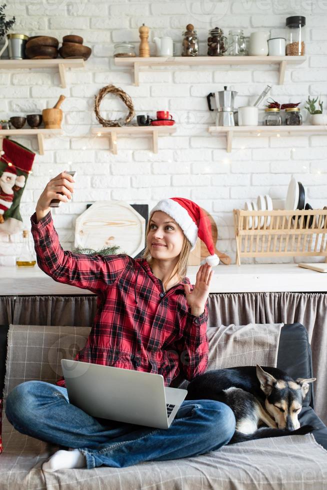 Mujer feliz con gorro de Papá Noel saludando a sus amigos en el chat de video en el portátil foto