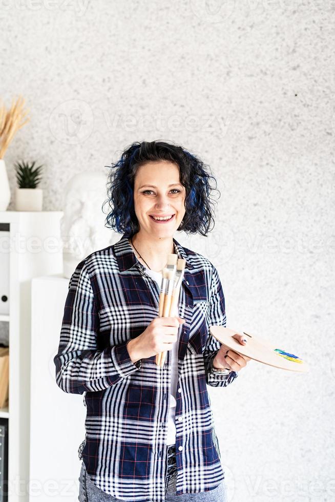 Artista mujer sonriente en su estudio sosteniendo paleta de arte foto