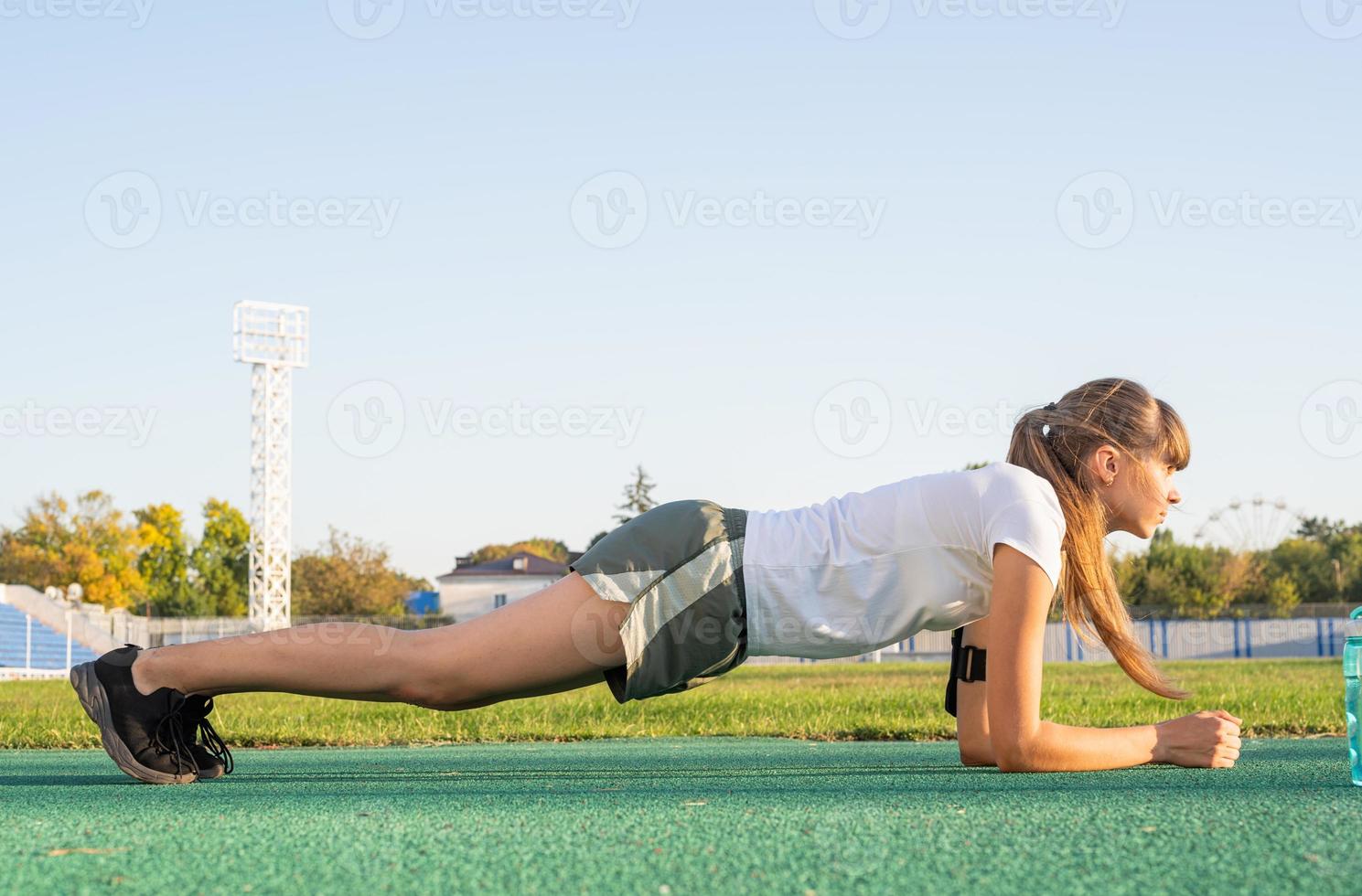 Chica adolescente en posición de plancha haciendo ejercicio en el estadio foto