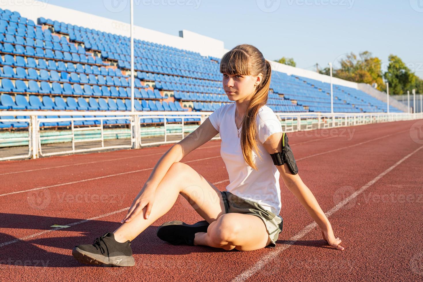 Teenager girl sitting on stadium track having rest photo